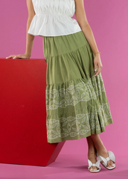 Person wearing a white top and green skirt with white patterns against a pink background